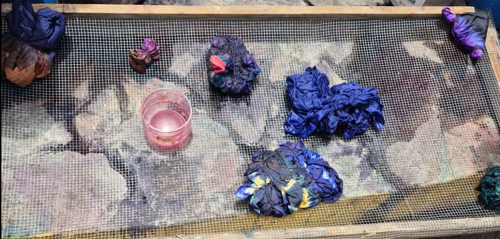 Freshly dyed Adire fabric bundles laid out to dry on a mesh rack at Charlestown Gallery